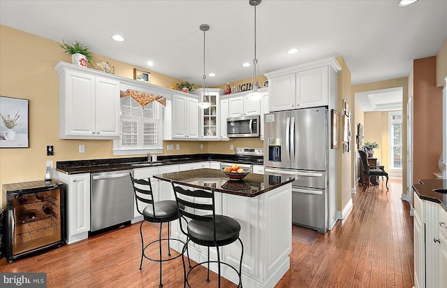 kitchen featuring appliances with stainless steel finishes, a kitchen island, decorative light fixtures, hardwood / wood-style floors, and white cabinetry