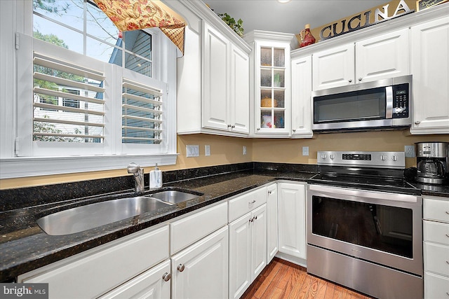 kitchen with white cabinets, appliances with stainless steel finishes, dark stone counters, and sink