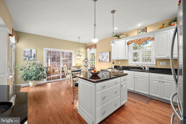 kitchen with sink, a kitchen island, light hardwood / wood-style flooring, pendant lighting, and white cabinets