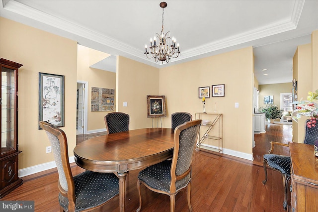 dining area with a raised ceiling, crown molding, dark wood-type flooring, and a notable chandelier