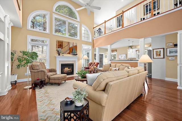 living room with decorative columns, ceiling fan, a towering ceiling, and hardwood / wood-style flooring