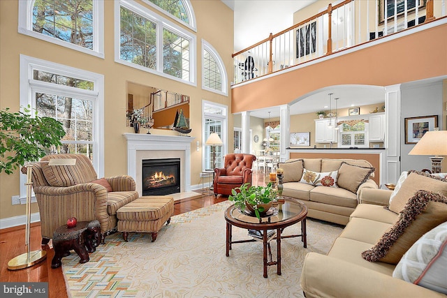 living room featuring plenty of natural light, a towering ceiling, light hardwood / wood-style flooring, and decorative columns