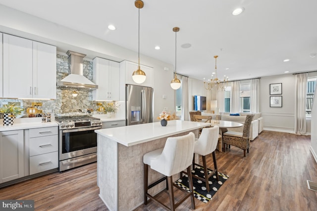 kitchen featuring decorative backsplash, hardwood / wood-style flooring, hanging light fixtures, appliances with stainless steel finishes, and custom range hood