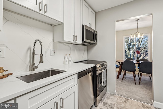 kitchen with light stone countertops, stainless steel appliances, sink, an inviting chandelier, and white cabinetry