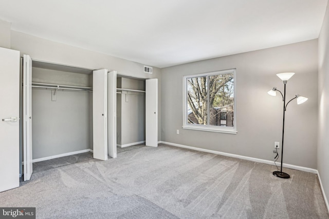 unfurnished bedroom featuring light colored carpet and multiple closets