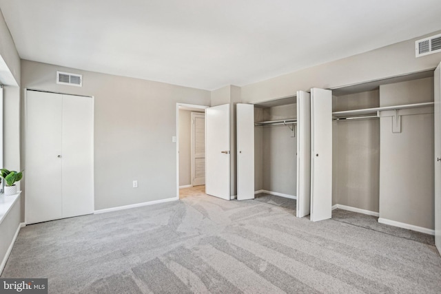 unfurnished bedroom with two closets and light colored carpet