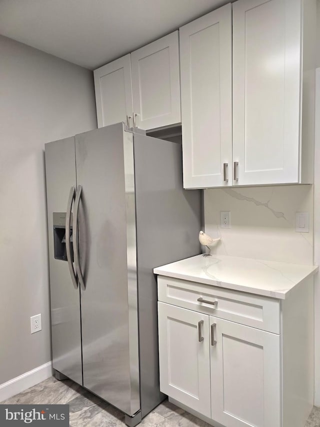 kitchen featuring stainless steel fridge, white cabinetry, and light stone counters