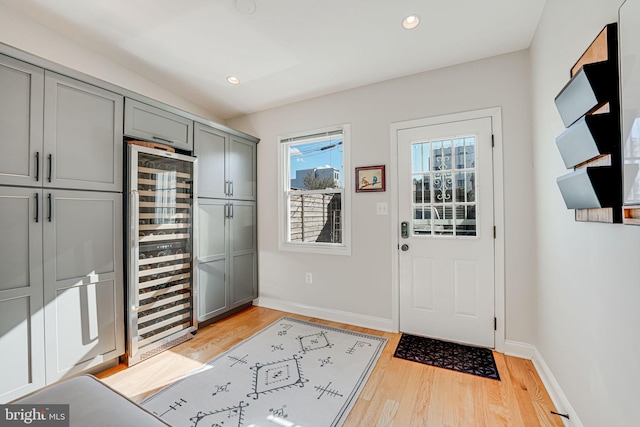 foyer entrance featuring baseboards, light wood finished floors, recessed lighting, and beverage cooler