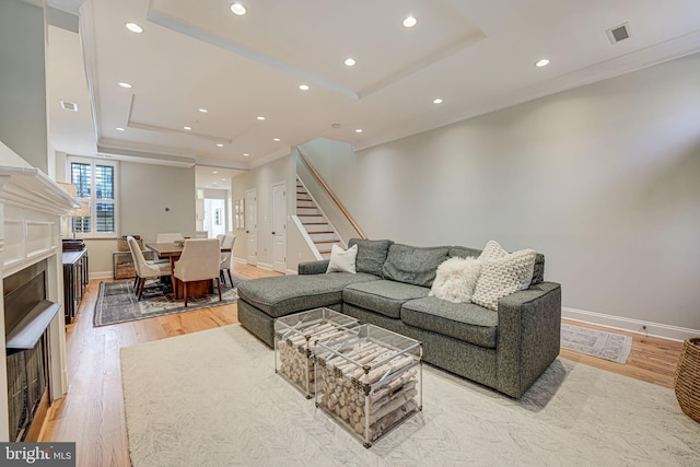living room with light wood finished floors, visible vents, stairway, and a raised ceiling