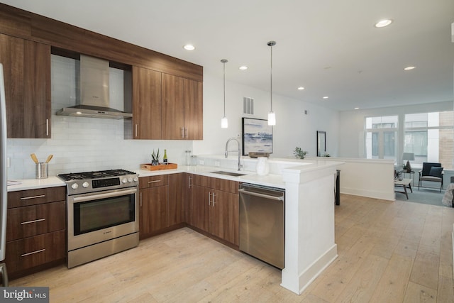 kitchen with sink, wall chimney exhaust hood, appliances with stainless steel finishes, light hardwood / wood-style floors, and kitchen peninsula