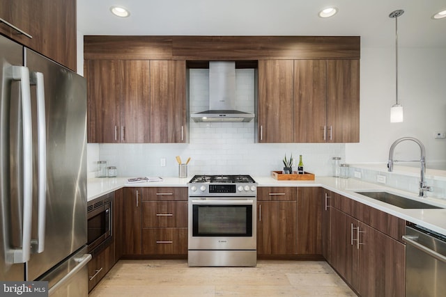 kitchen with pendant lighting, sink, wall chimney exhaust hood, light wood-type flooring, and stainless steel appliances