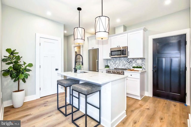 kitchen with hanging light fixtures, stainless steel appliances, a breakfast bar, a kitchen island with sink, and white cabinetry