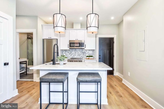 kitchen featuring white cabinets, a kitchen island with sink, pendant lighting, and appliances with stainless steel finishes