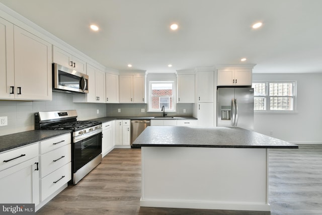 kitchen featuring a sink, stainless steel appliances, dark countertops, and a kitchen island