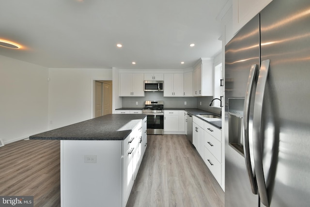 kitchen featuring white cabinets, dark countertops, a kitchen island, appliances with stainless steel finishes, and a sink