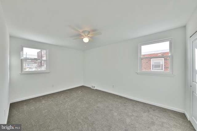 spare room featuring ceiling fan, dark carpet, visible vents, and baseboards