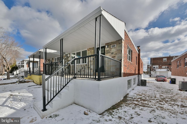 view of snowy exterior with central AC unit and a residential view