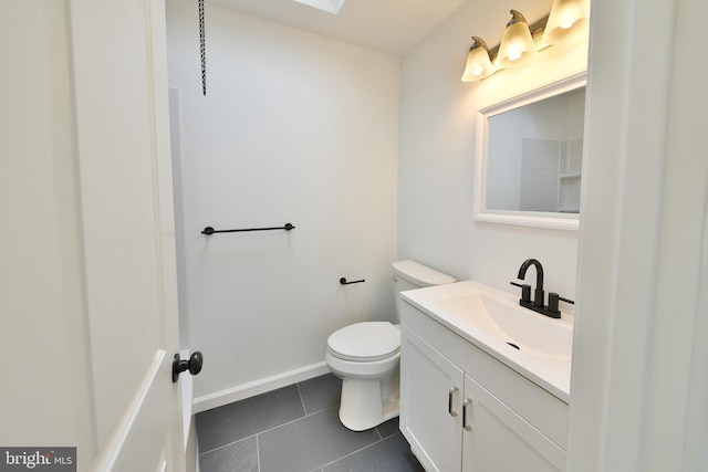 bathroom with toilet, a skylight, vanity, baseboards, and tile patterned floors