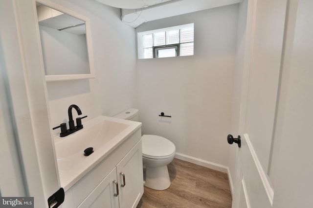 half bathroom with baseboards, vanity, toilet, and wood finished floors