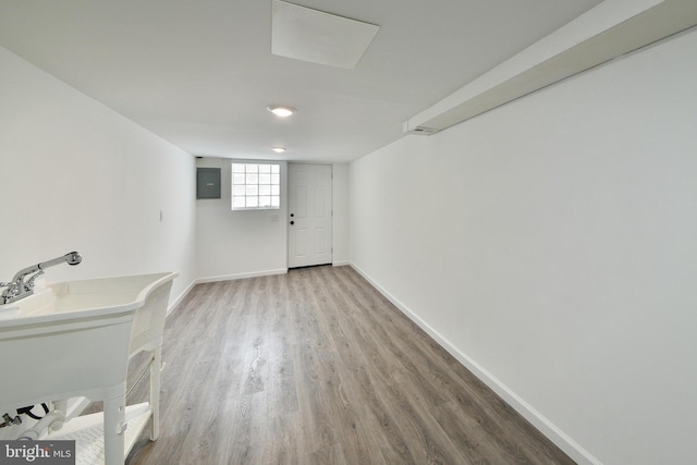 below grade area featuring electric panel, a sink, baseboards, and wood finished floors