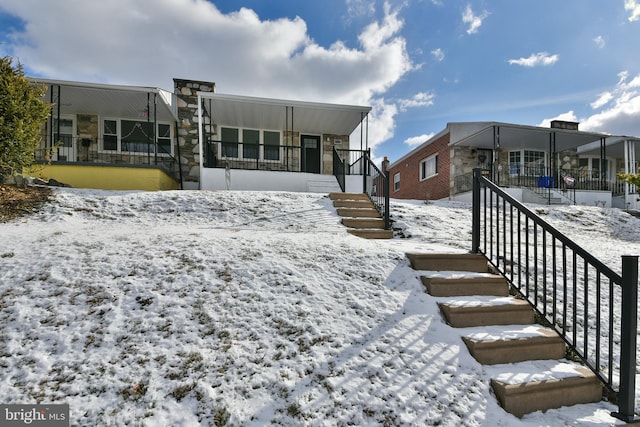 snow covered house featuring a porch and stairs