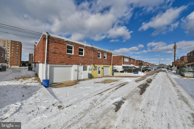 snow covered house featuring brick siding, an attached garage, and central AC unit