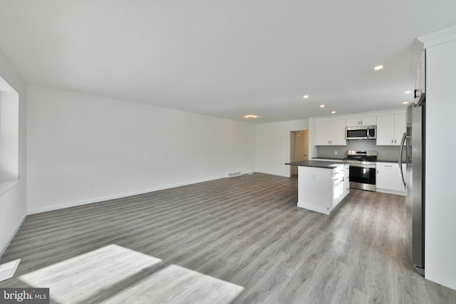 kitchen featuring a center island, dark countertops, appliances with stainless steel finishes, open floor plan, and white cabinets