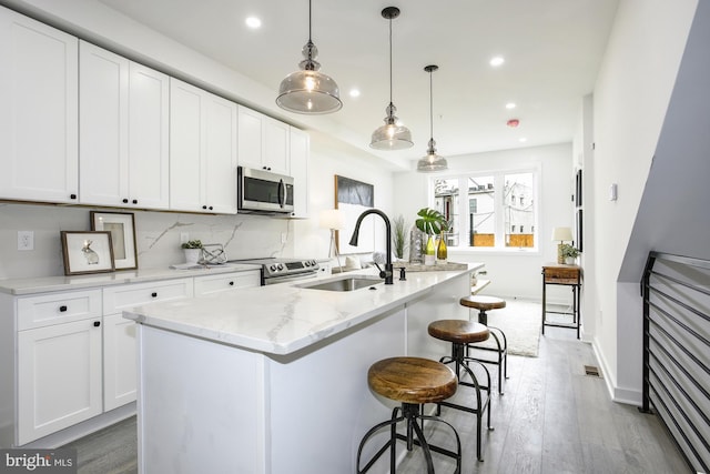 kitchen with appliances with stainless steel finishes, a center island with sink, and white cabinetry