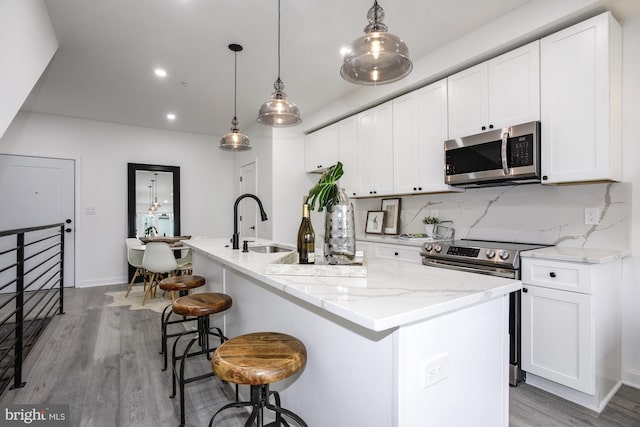 kitchen featuring white cabinets, hanging light fixtures, an island with sink, and appliances with stainless steel finishes