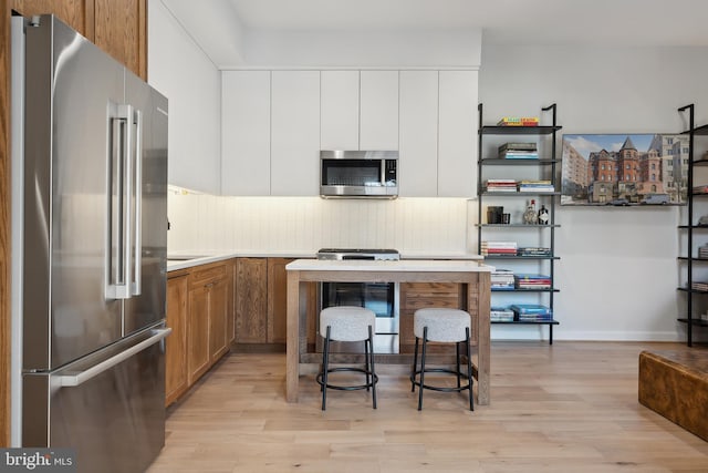 kitchen with stainless steel appliances, light countertops, light wood-type flooring, white cabinetry, and backsplash