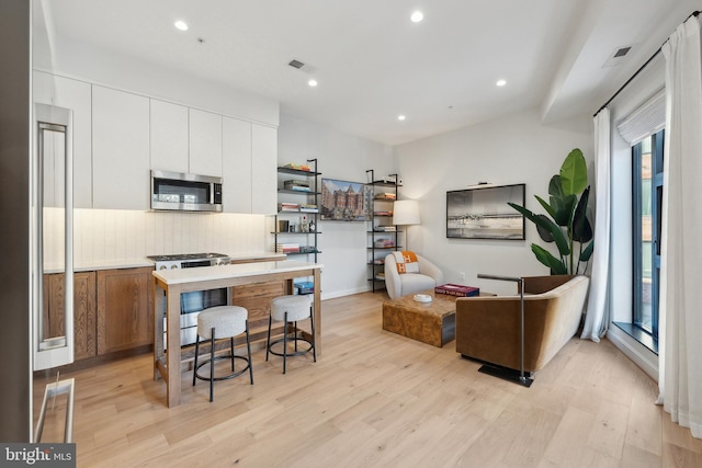 kitchen with visible vents, white cabinets, decorative backsplash, light wood-style flooring, and appliances with stainless steel finishes