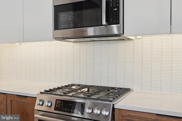 kitchen with stainless steel appliances, light stone counters, backsplash, and brown cabinets