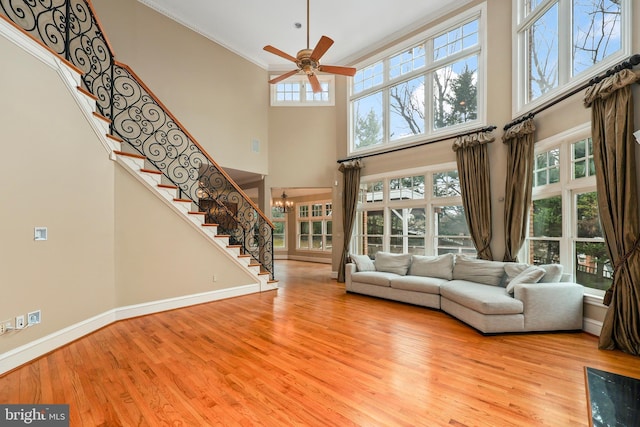 unfurnished living room with a high ceiling, ceiling fan with notable chandelier, a wealth of natural light, and light wood-type flooring