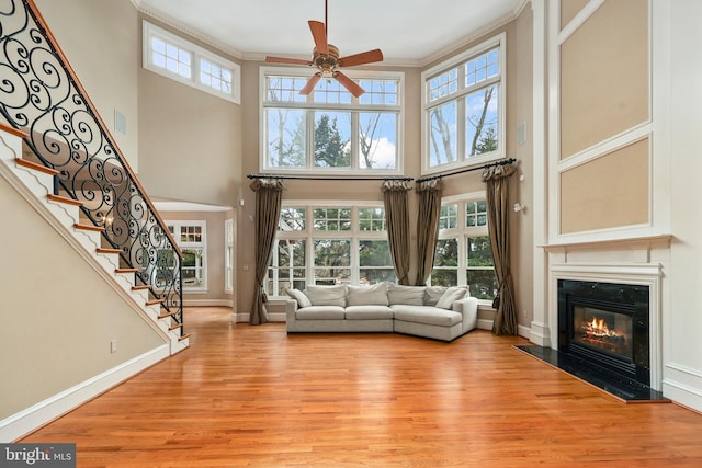 unfurnished living room featuring crown molding, a towering ceiling, light hardwood / wood-style floors, and ceiling fan