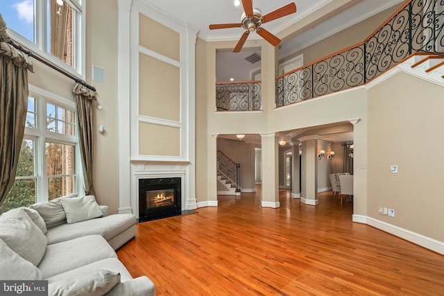 living room featuring hardwood / wood-style flooring, a premium fireplace, ceiling fan, a towering ceiling, and decorative columns