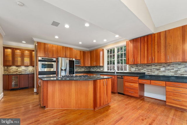 kitchen with appliances with stainless steel finishes, built in desk, a kitchen island, and light wood-type flooring