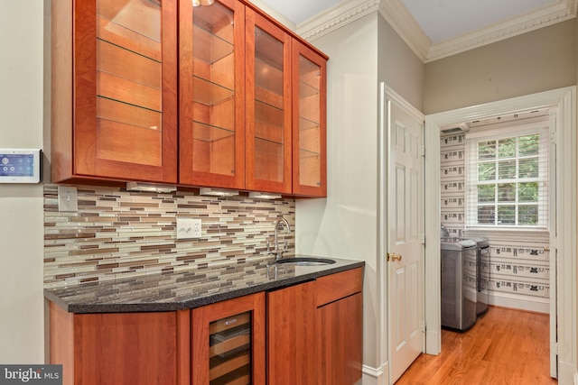 bar featuring sink, dark stone countertops, backsplash, washing machine and dryer, and light hardwood / wood-style floors