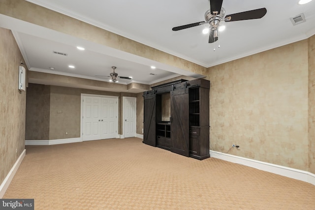 unfurnished living room featuring crown molding, a barn door, ceiling fan, and carpet flooring