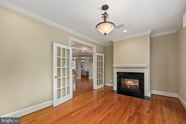 unfurnished living room featuring hardwood / wood-style floors, a premium fireplace, ornamental molding, and french doors