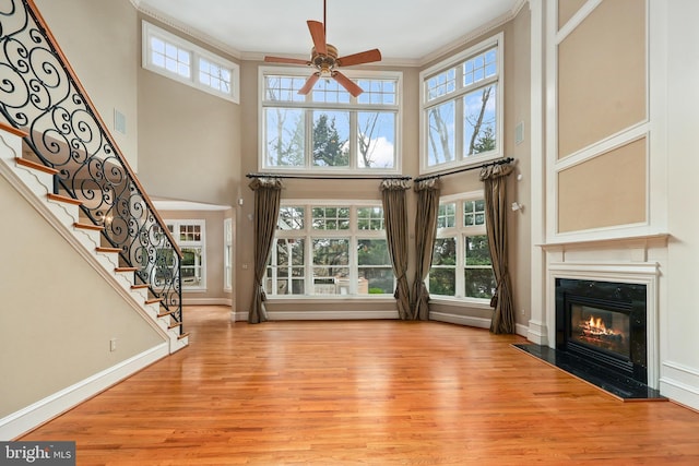 unfurnished living room with crown molding, a towering ceiling, ceiling fan, and light wood-type flooring