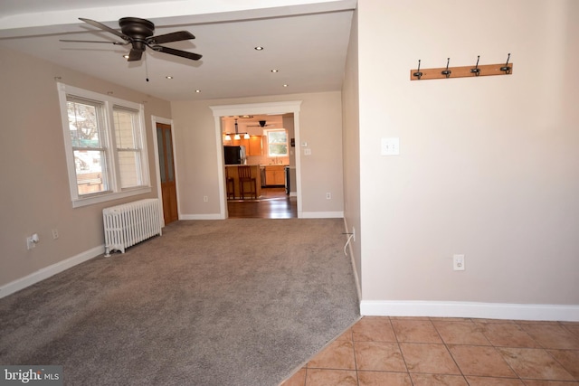 unfurnished living room with radiator heating unit, light colored carpet, and ceiling fan