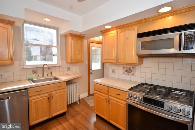 kitchen featuring radiator, sink, tasteful backsplash, appliances with stainless steel finishes, and light wood-type flooring