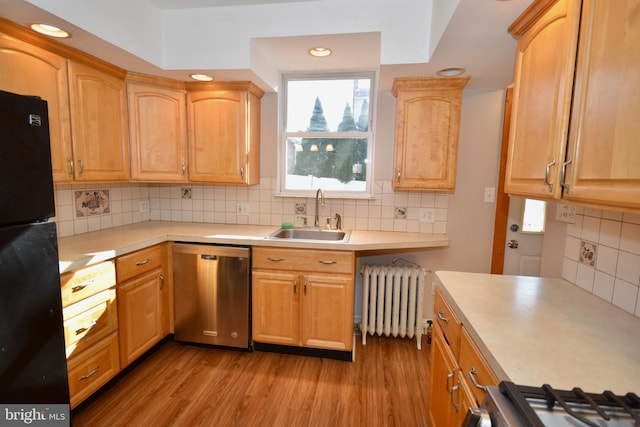 kitchen featuring black refrigerator, light wood-type flooring, stainless steel dishwasher, sink, and radiator heating unit