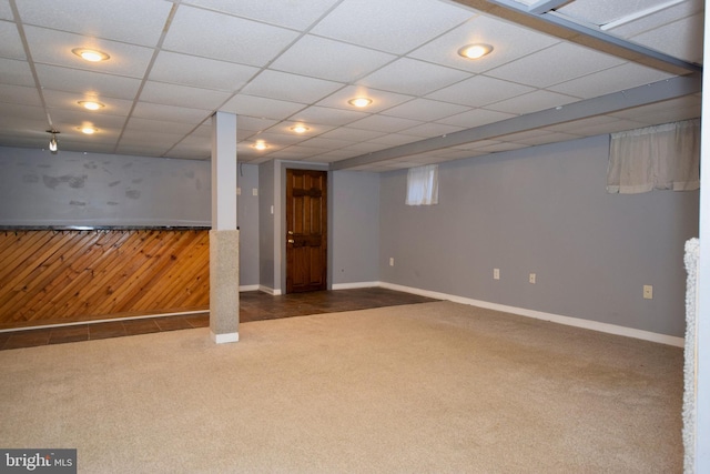 basement featuring wooden walls, a drop ceiling, and carpet floors