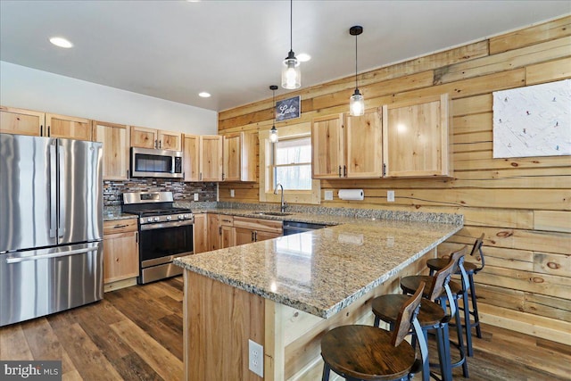 kitchen with light stone countertops, appliances with stainless steel finishes, light brown cabinets, sink, and hanging light fixtures