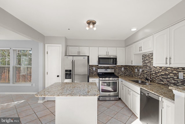 kitchen featuring light stone counters, a kitchen island, white cabinetry, appliances with stainless steel finishes, and sink