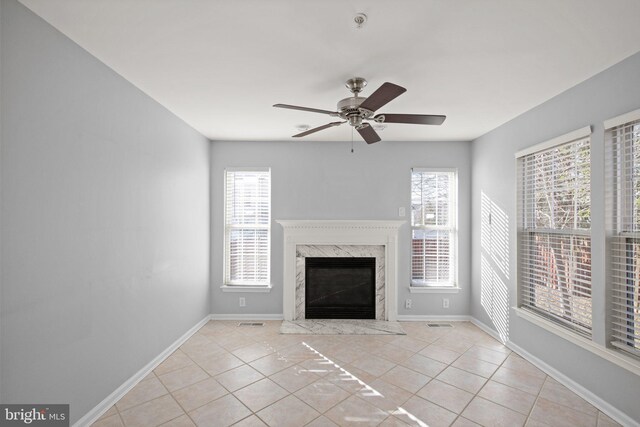 unfurnished living room with ceiling fan, light tile patterned flooring, and a high end fireplace