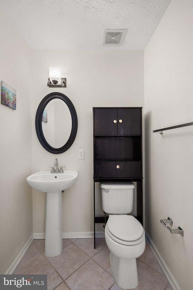 bathroom with a textured ceiling, sink, tile patterned floors, and toilet