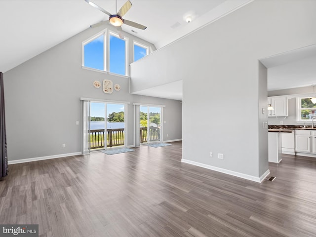 unfurnished living room with hardwood / wood-style floors, ceiling fan, a water view, and a high ceiling