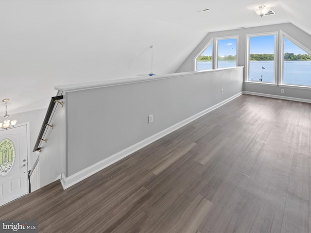 additional living space featuring an inviting chandelier, a water view, vaulted ceiling, and dark wood-type flooring